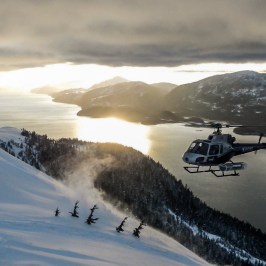 a helicopter flying over a river and snow covered mountain