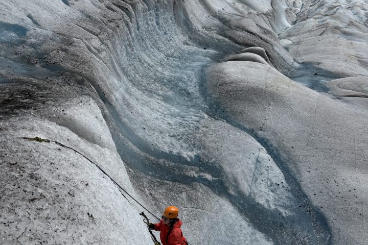 Two climbers ascend a steep, icy glacier with equipment and ropes.