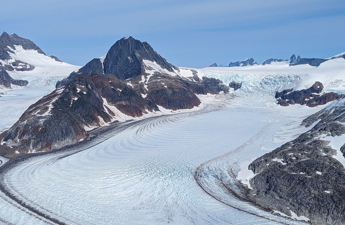Mountain landscape with glacier flowing between rocky peaks under blue sky.